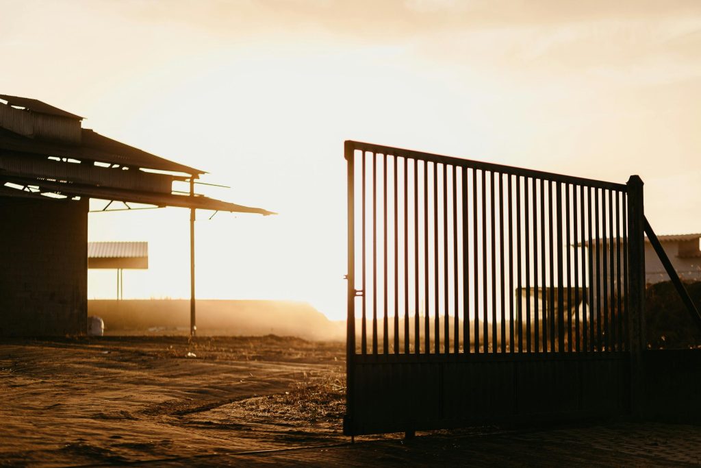 Industrial landscape with a metal gate silhouetted against a sunset sky, exuding a warm, rustic ambiance.